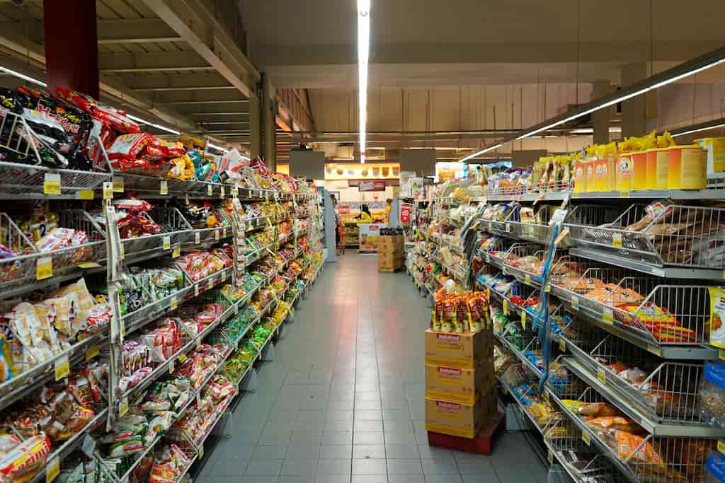 Interior of a grocery store aisle lined with shelves of packaged snacks and goods, bright fluorescent lighting
